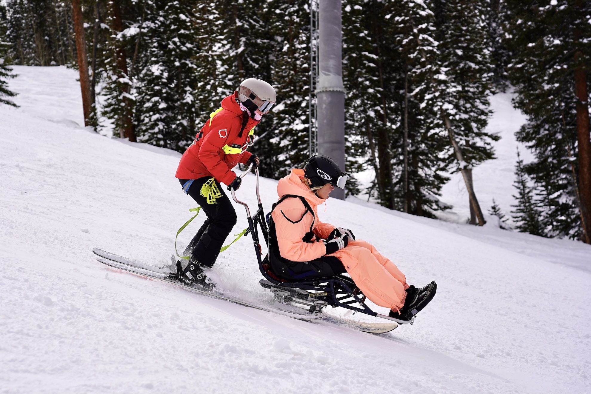 A ski instructor in red bucketing a sitskier down the hill